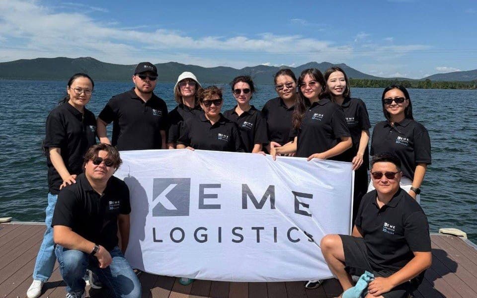 Команда KEME Logistics с фирменным баннером на берегу озера в День железнодорожника